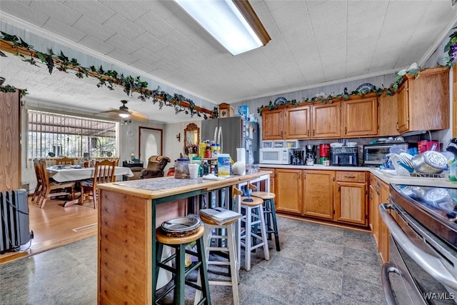 kitchen with stainless steel appliances, ceiling fan, crown molding, and a breakfast bar area