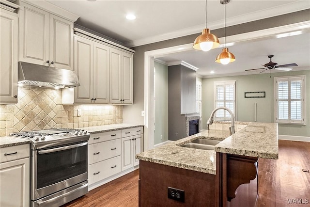 kitchen with ceiling fan, sink, light stone countertops, stainless steel range with gas cooktop, and a center island with sink