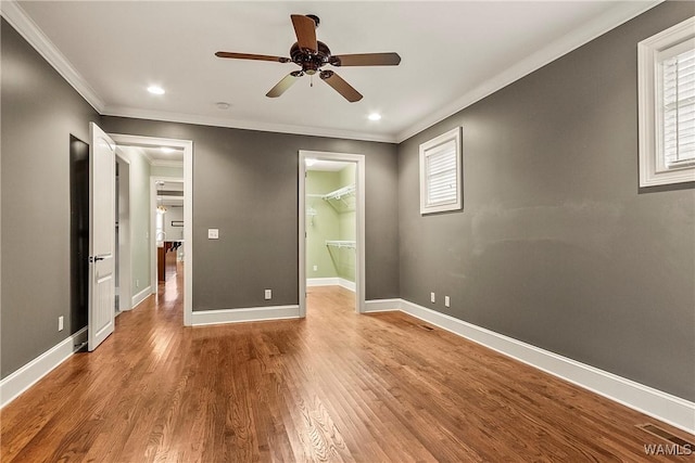 unfurnished bedroom featuring light wood-type flooring, ceiling fan, crown molding, a spacious closet, and a closet