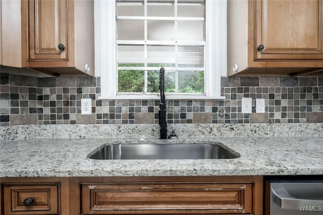 4205 Cloverdale Est, Northport, AL 35473 - kitchen featuring a sink, brown cabinets, stainless steel dishwasher, tasteful backsplash, and light stone counters