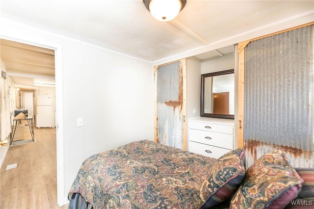 bedroom with a textured ceiling, white fridge, and light hardwood / wood-style flooring