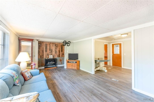 unfurnished living room featuring hardwood / wood-style floors, a paneled ceiling, a wood stove, wooden walls, and ornamental molding