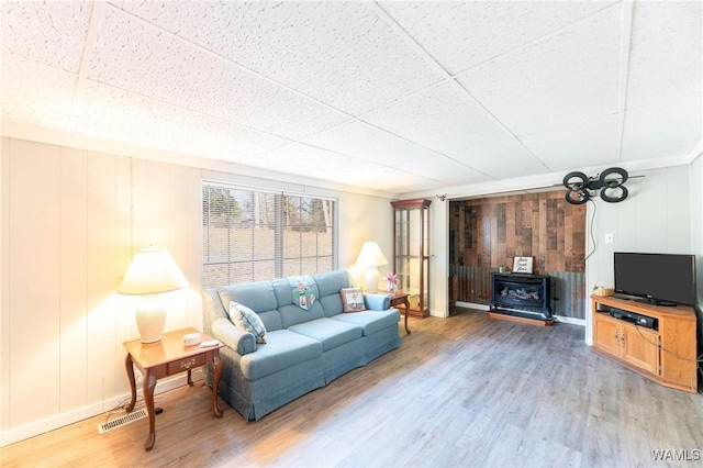 living room with a paneled ceiling, wooden walls, wood-type flooring, and a wood stove