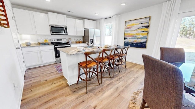 kitchen featuring light stone countertops, white cabinetry, light hardwood / wood-style flooring, and stainless steel appliances