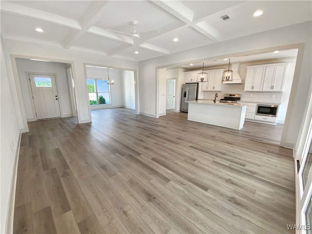 unfurnished living room featuring light wood-type flooring, coffered ceiling, ceiling fan, sink, and beam ceiling