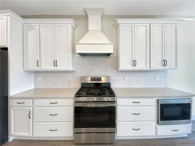 kitchen with built in microwave, white cabinets, custom range hood, and stainless steel gas range