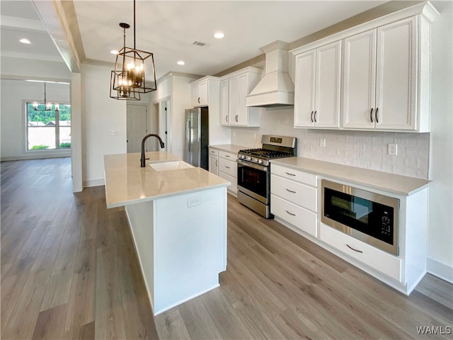 kitchen featuring premium range hood, sink, decorative light fixtures, white cabinetry, and stainless steel appliances