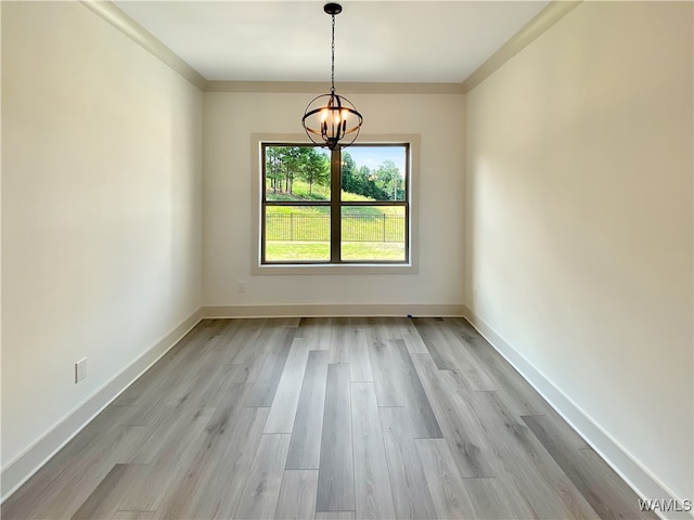 spare room with crown molding, an inviting chandelier, and light wood-type flooring