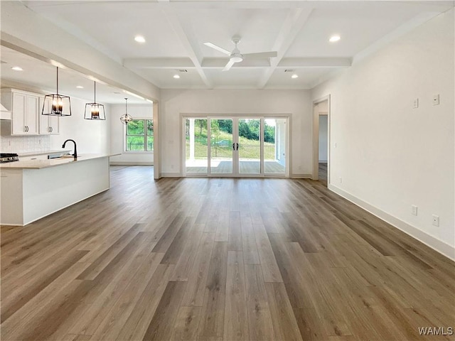 unfurnished living room with dark hardwood / wood-style flooring, coffered ceiling, ceiling fan with notable chandelier, sink, and beamed ceiling