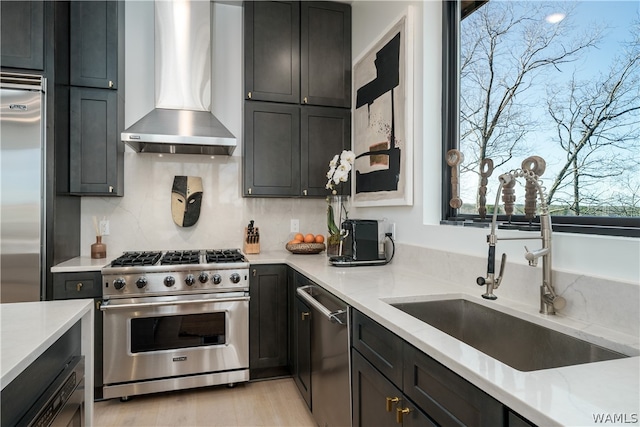 kitchen with decorative backsplash, light stone countertops, high end appliances, sink, and wall chimney range hood