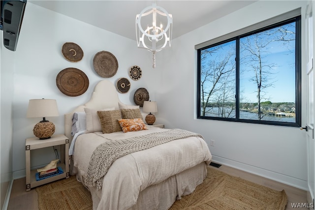 bedroom featuring a water view, wood-type flooring, and a notable chandelier