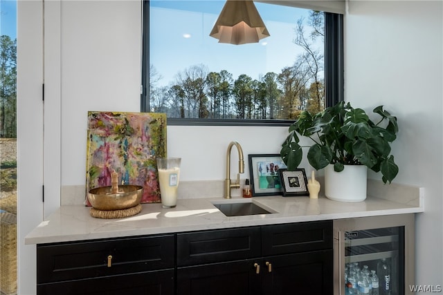 bar featuring a wealth of natural light, light stone counters, beverage cooler, and sink