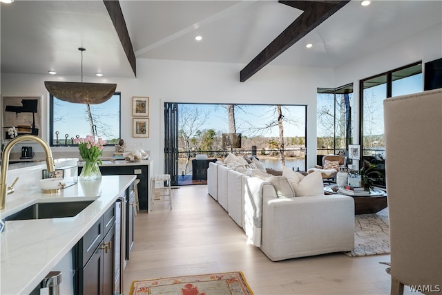 kitchen featuring beam ceiling, light stone countertops, sink, light hardwood / wood-style floors, and decorative light fixtures