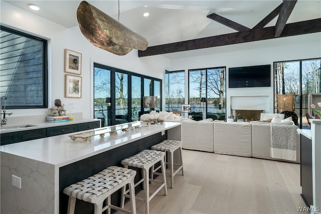 kitchen with sink, light stone counters, light hardwood / wood-style flooring, pendant lighting, and a breakfast bar