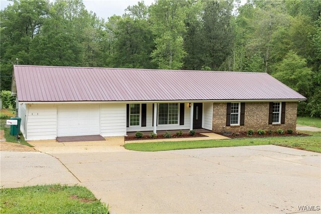 ranch-style house featuring a garage, a front lawn, covered porch, metal roof, and driveway