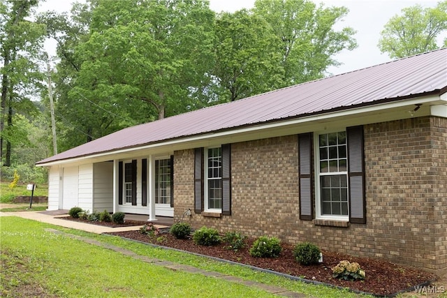 view of front of property with brick siding, a front yard, and metal roof