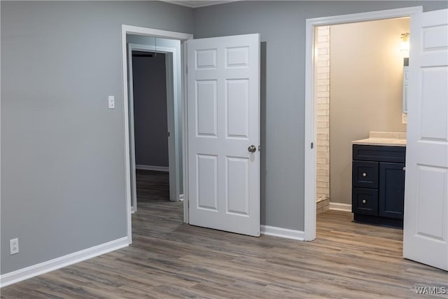 unfurnished bedroom with baseboards, wood finished floors, and ensuite bath