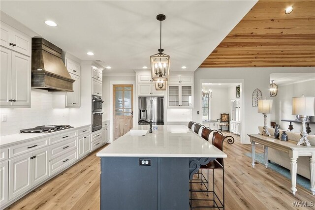 17505 Mormon Rd, Northport, AL 35475 - kitchen featuring premium range hood, appliances with stainless steel finishes, a kitchen bar, white cabinetry, and decorative backsplash