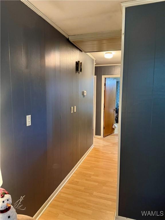 corridor with wood walls, ornamental molding, and light wood-type flooring