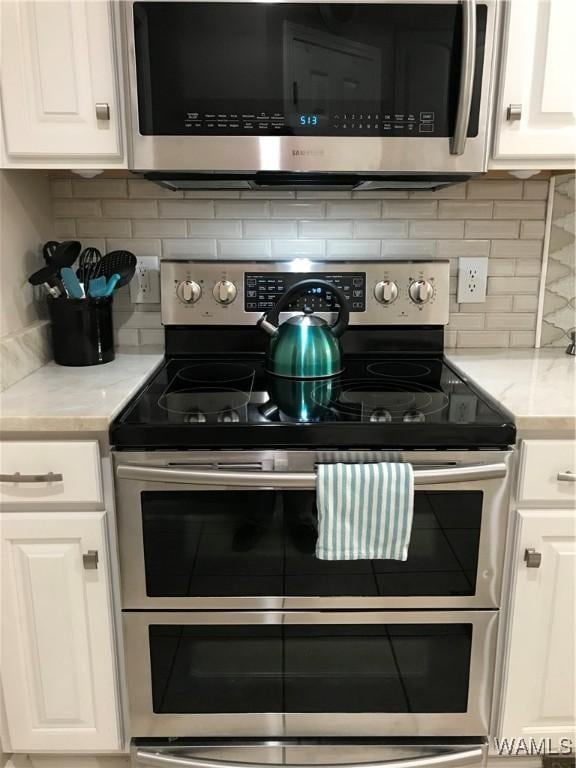 kitchen with tasteful backsplash, appliances with stainless steel finishes, light stone countertops, and white cabinets