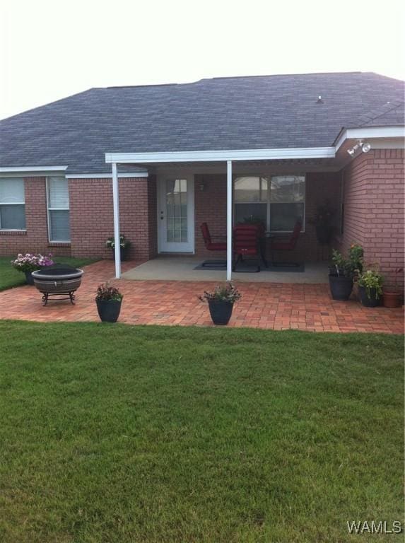 back of property with a shingled roof, brick siding, and a lawn