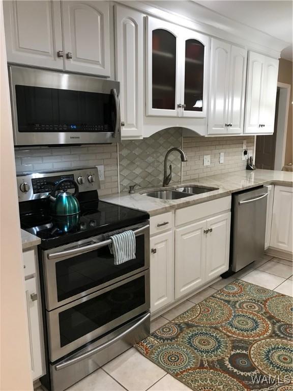 kitchen featuring stainless steel appliances, light tile patterned flooring, a sink, and white cabinets