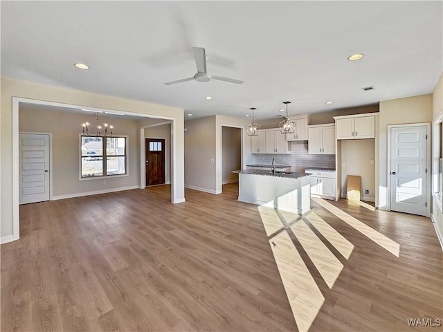 kitchen with white cabinetry, a kitchen island with sink, pendant lighting, and light wood-type flooring