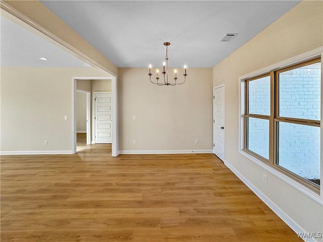 spare room with a notable chandelier and light hardwood / wood-style floors