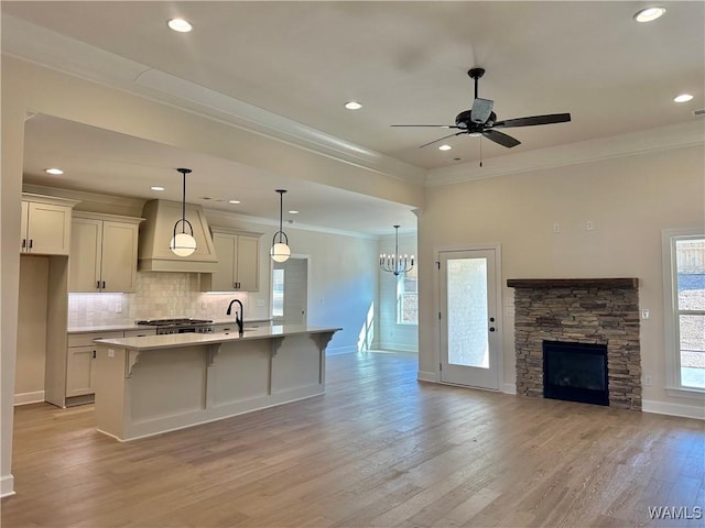 kitchen with a wealth of natural light, custom range hood, a kitchen island with sink, and hanging light fixtures