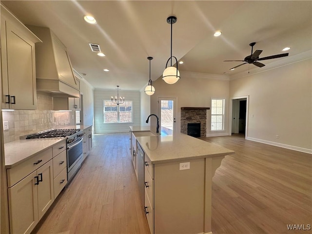 kitchen with high end range, premium range hood, light stone counters, pendant lighting, and a center island with sink