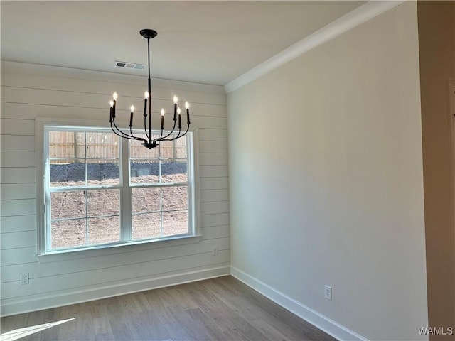 unfurnished dining area featuring a chandelier, wood-type flooring, and crown molding