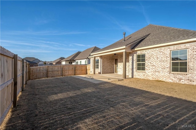 back of house with brick siding, roof with shingles, a fenced backyard, a patio area, and a ceiling fan