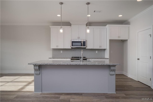 kitchen featuring stainless steel microwave, white cabinetry, crown molding, and visible vents