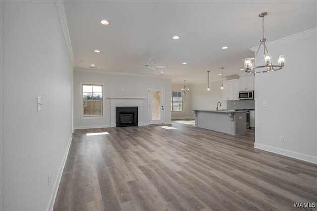 unfurnished living room with a glass covered fireplace, wood finished floors, recessed lighting, crown molding, and baseboards