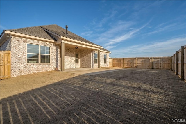 rear view of house with ceiling fan, roof with shingles, a fenced backyard, and a patio area