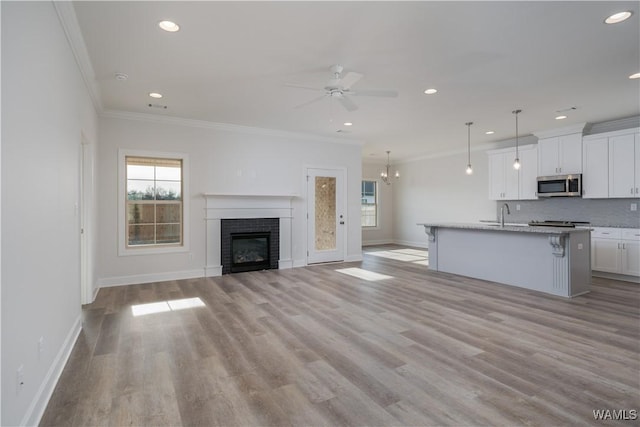 unfurnished living room featuring crown molding, baseboards, ceiling fan, a fireplace, and light wood-style floors