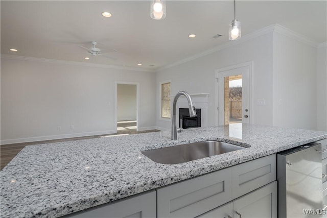 kitchen featuring light stone counters, dishwashing machine, crown molding, and a sink