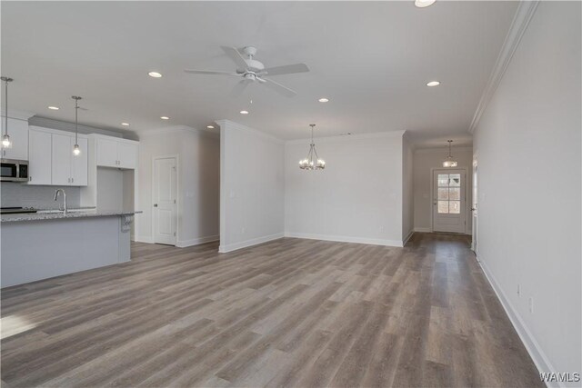 unfurnished living room featuring ceiling fan with notable chandelier, wood finished floors, and baseboards