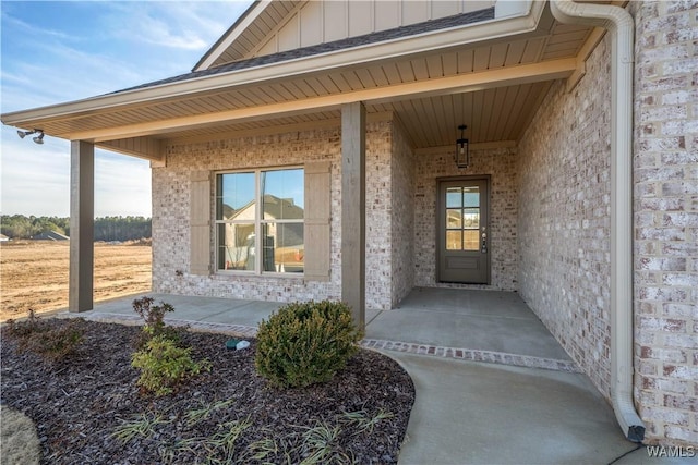 entrance to property featuring a porch, brick siding, and board and batten siding