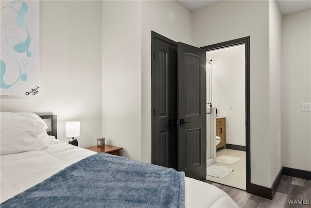 bedroom with ensuite bathroom, dark wood-type flooring, and baseboards