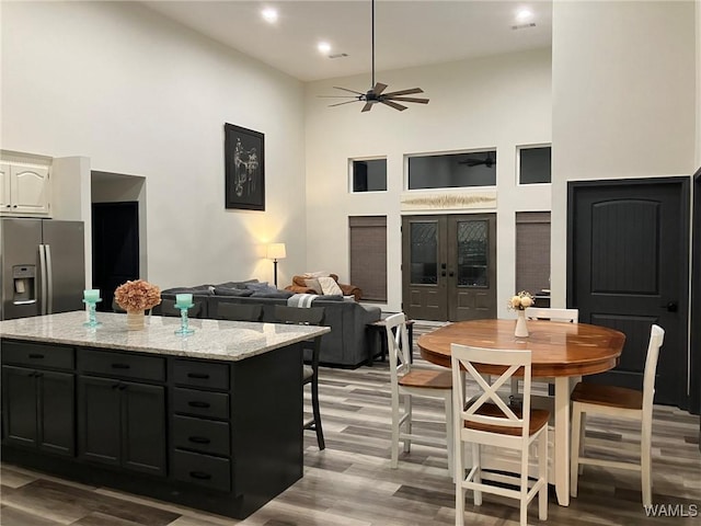 kitchen with stainless steel fridge, a towering ceiling, a kitchen island, light stone counters, and open floor plan