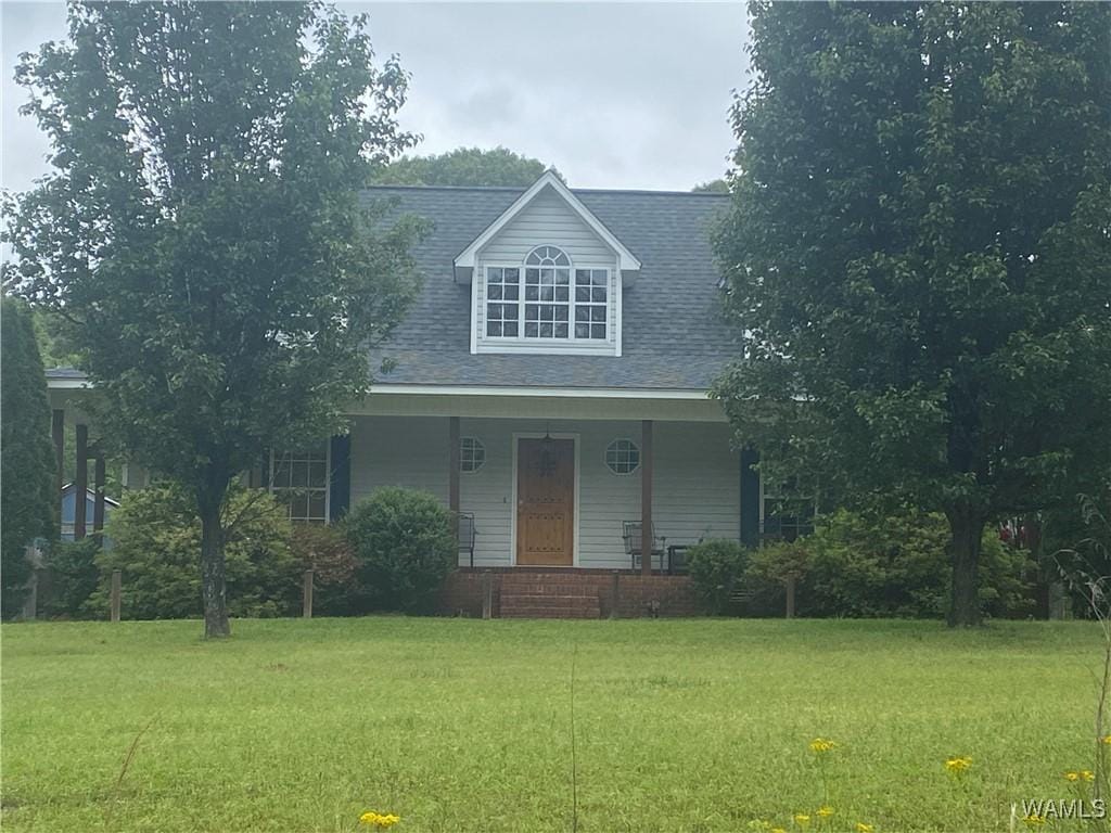 new england style home featuring covered porch, a shingled roof, and a front lawn