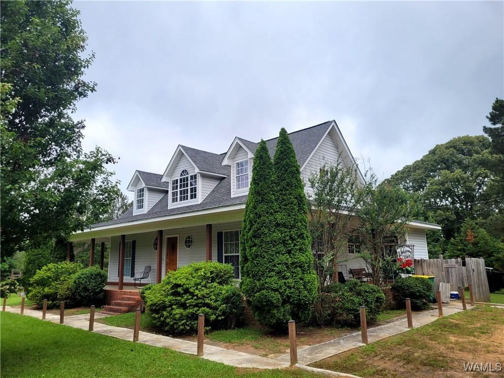 cape cod-style house with covered porch, fence, a shingled roof, and a front yard