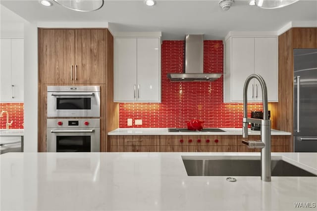 kitchen featuring sink, tasteful backsplash, white cabinets, stainless steel appliances, and wall chimney range hood