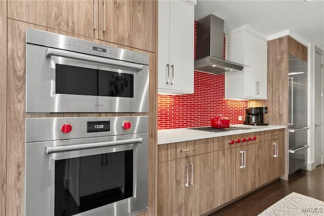 kitchen featuring wall chimney range hood, appliances with stainless steel finishes, dark hardwood / wood-style floors, white cabinets, and decorative backsplash