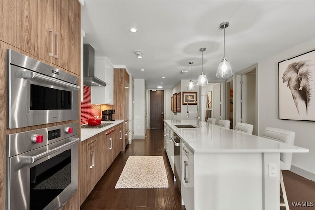 kitchen with sink, a center island with sink, a kitchen breakfast bar, wall chimney range hood, and backsplash