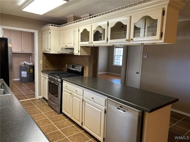 kitchen featuring decorative backsplash, dark countertops, a peninsula, stainless steel appliances, and under cabinet range hood