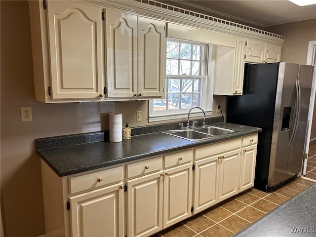 kitchen featuring stainless steel fridge, dark countertops, cream cabinets, dark tile patterned floors, and a sink