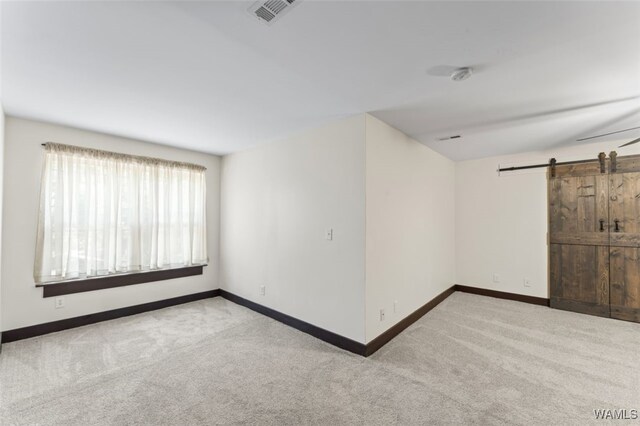 carpeted spare room featuring ceiling fan and a barn door