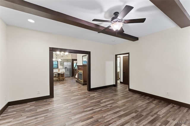 spare room featuring beam ceiling, hardwood / wood-style floors, and ceiling fan with notable chandelier